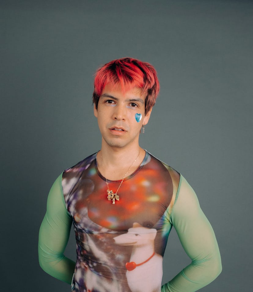 A person with pink hair and a blue heart face tattoo wears a colorful, form-fitting top with a whims...