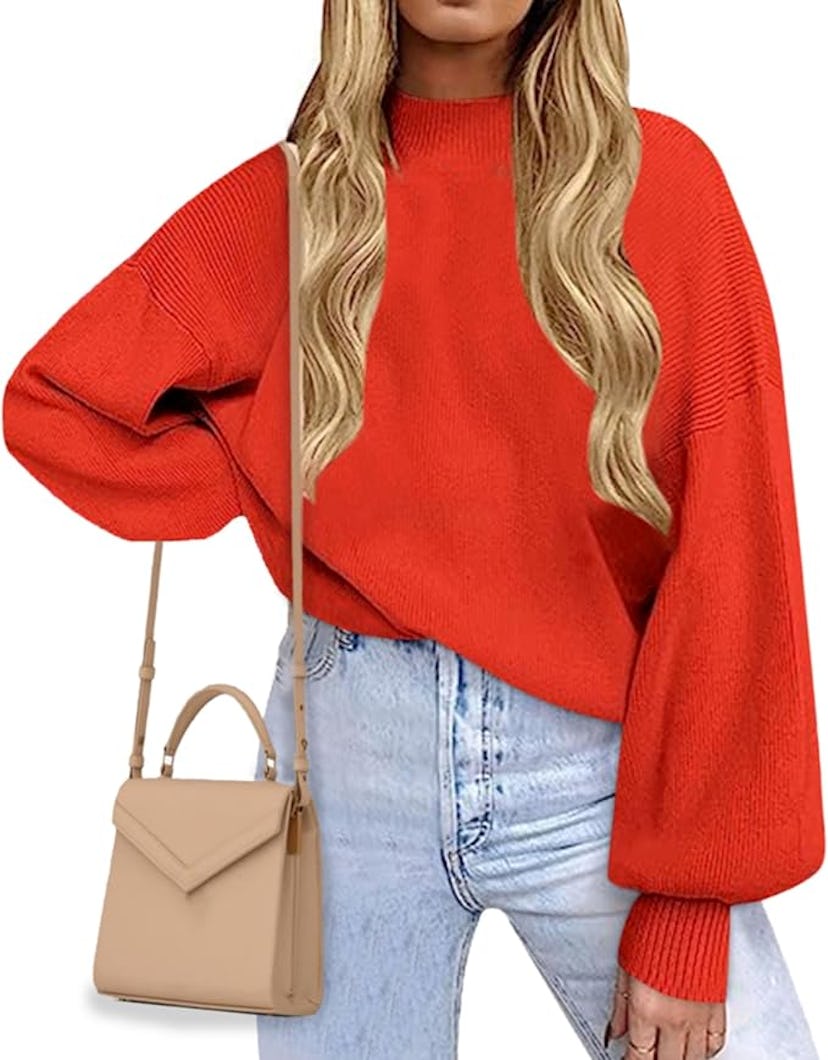 A person wearing a bright red oversized sweater and light blue jeans, holding a beige handbag, with ...