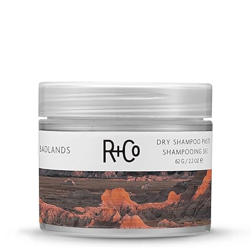 A clear jar of R+Co Badlands dry shampoo paste with a scenic label featuring a colorful desert lands...