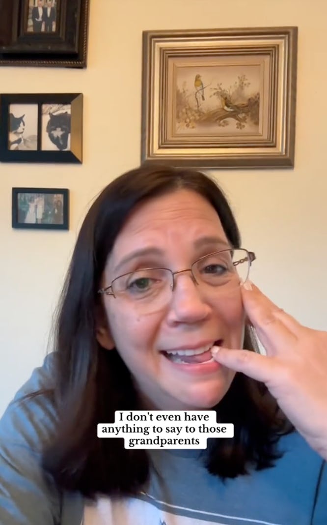 A woman with glasses smiles while speaking on the phone. She gestures expressively with her hand, sitting in a room with framed artwork on the wall.