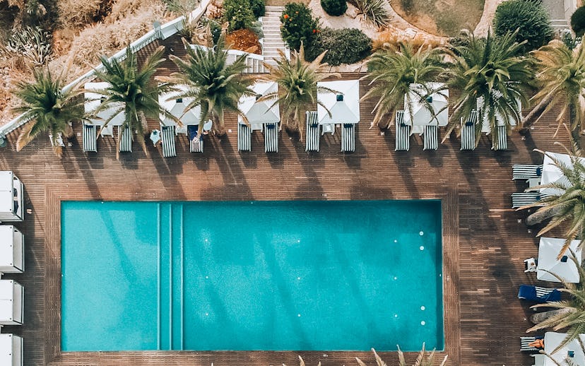 Aerial view of a serene swimming pool surrounded by palm trees and lounge chairs, set against a back...