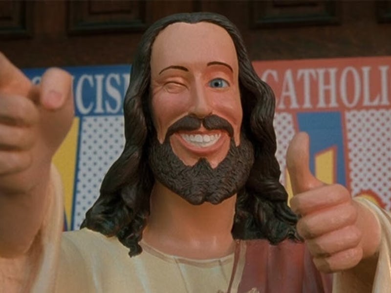 A whimsical statue depicting a smiling, winking figure with long hair and a beard, giving a thumbs-u...