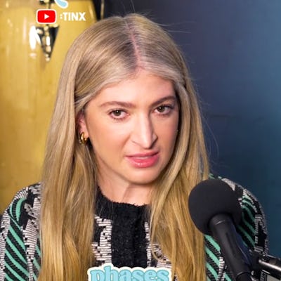 A woman with long blonde hair sits at a microphone, expressing a thoughtful demeanor. The backdrop includes musical instruments and the text