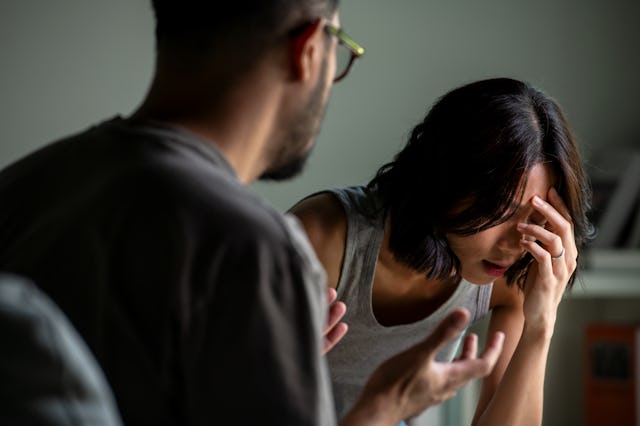 A man gestures animatedly while speaking to a woman who appears distressed, holding her head in her ...