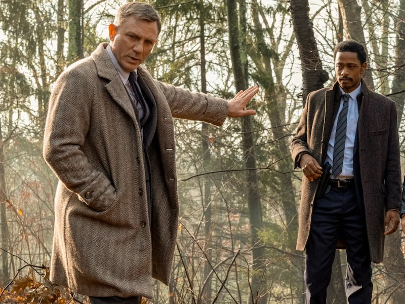 Three detectives are outdoors in a wooded area, discussing a case. One man gestures while the others...