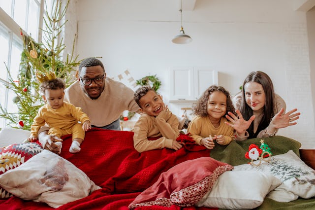 A family of five, including two adults and three children, smiles and poses playfully on a couch wit...
