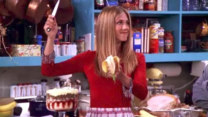 A woman with long hair holds a knife in one hand and a banana in the other, smiling playfully in a c...