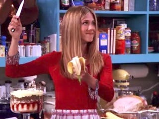 A woman with long hair holds a knife in one hand and a banana in the other, smiling playfully in a c...