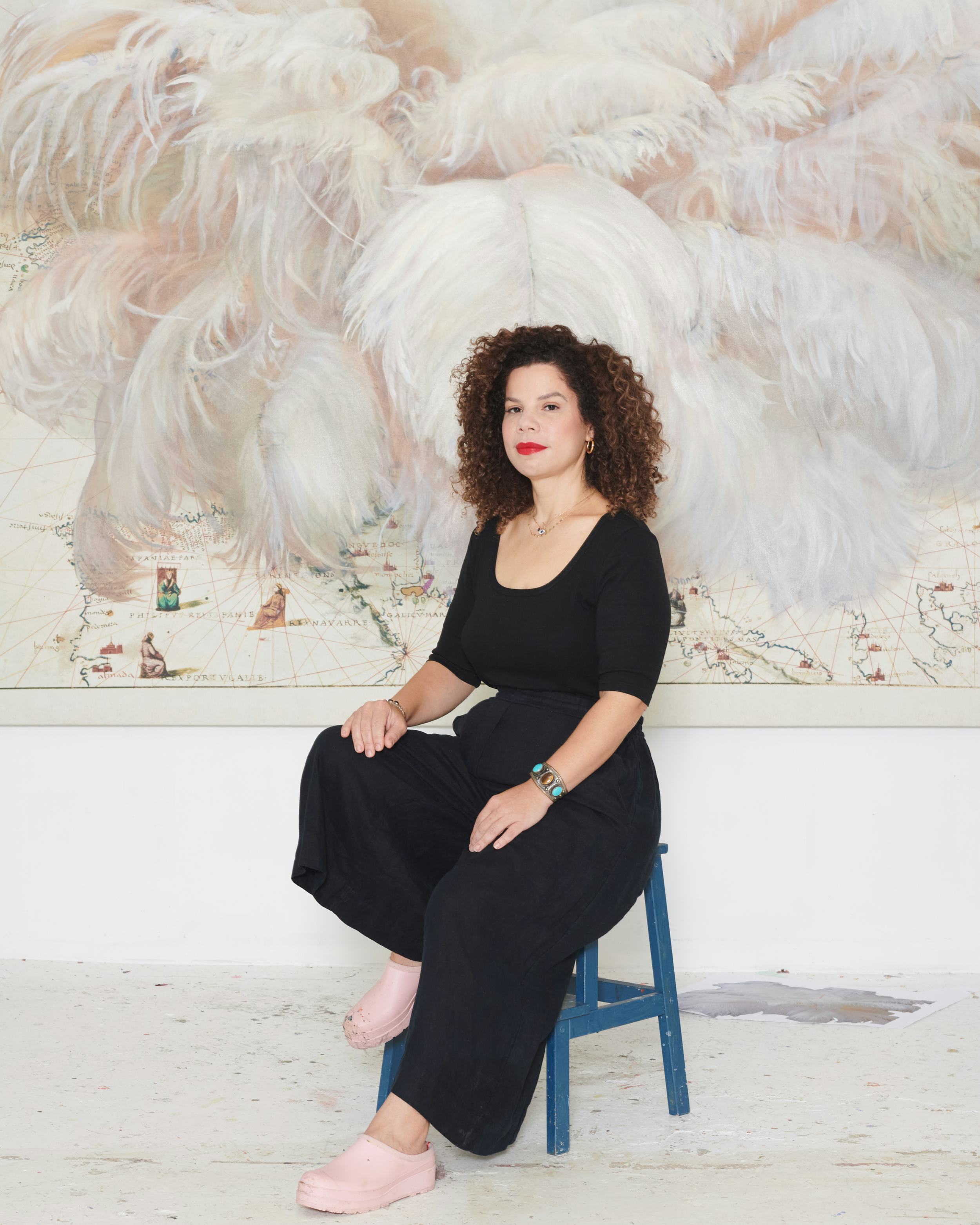 Firelei Báez sitting in front of one of her works