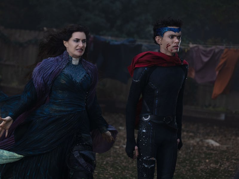 A woman in a dark, flowing gown gestures dramatically alongside a young man in a superhero outfit wi...