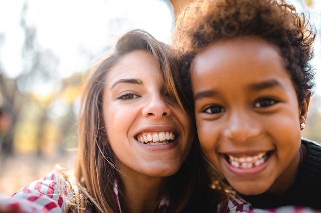A woman and a young child smile joyfully at the camera, showcasing their happiness in a sunny outdoo...