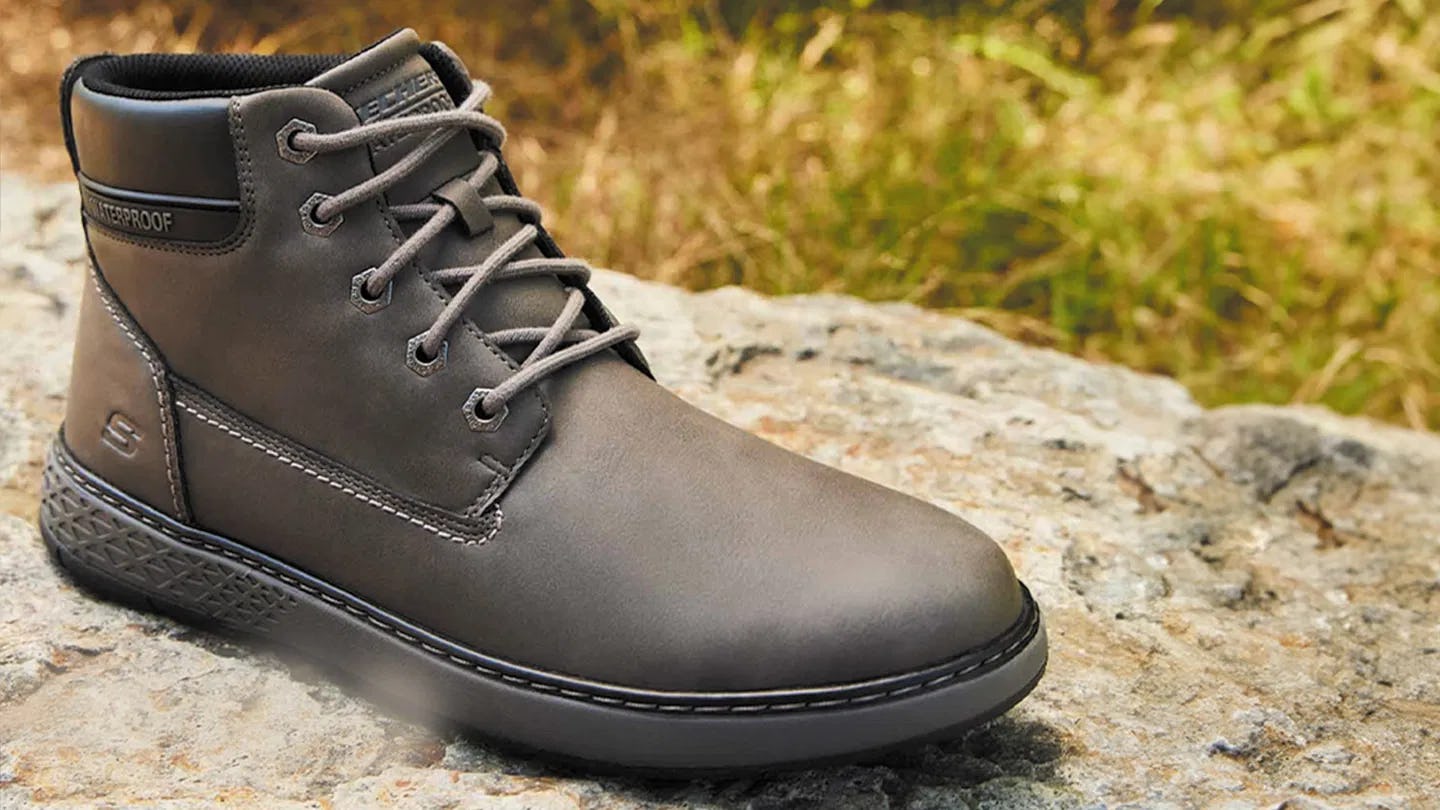A stylish hiking boot sits on a rock, featuring laces and a textured sole, set against a natural bac...