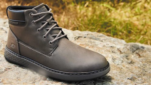 A stylish hiking boot sits on a rock, featuring laces and a textured sole, set against a natural bac...