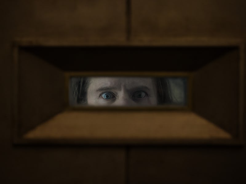 A close-up view through a narrow peephole reveals a pair of intense blue eyes, surrounded by slightl...