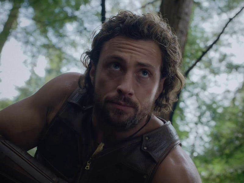 A man with curly brown hair and a rugged appearance looks thoughtfully upwards while sitting on the ...