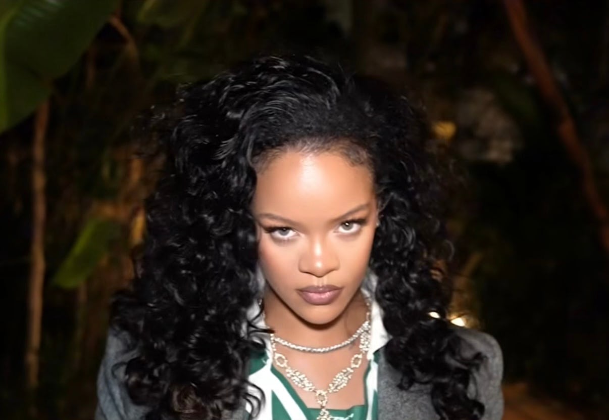 RRihanna wears a gray pantsuit, soccer shirt, and diamond necklaces.