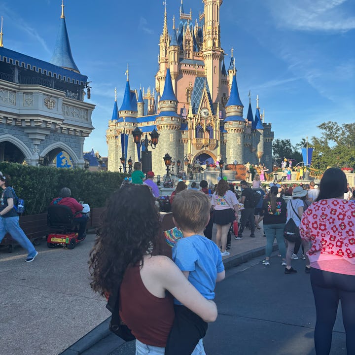 A mom holds her son watching a performance in front of cinderella's castle at magic kingdom.