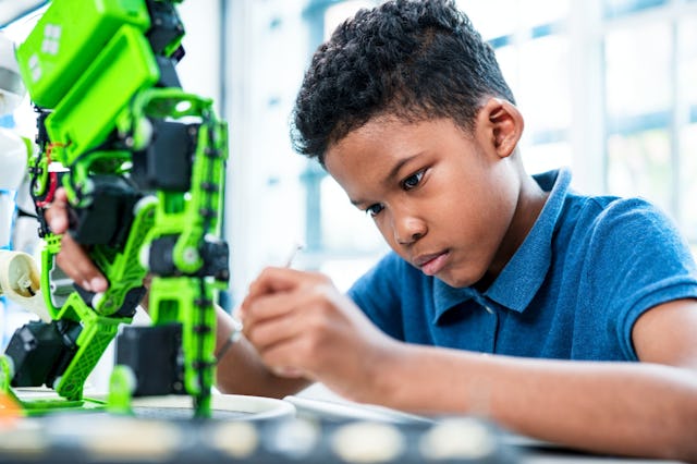 A focused boy carefully works on assembling a green robotic arm, showcasing creativity and concentra...