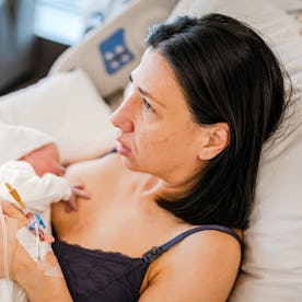 A mother tenderly holds her newborn baby while breastfeeding in a hospital bed. She looks calm and r...