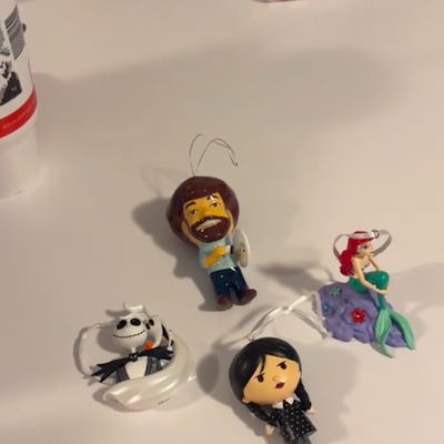 A collection of colorful holiday ornaments featuring a cartoon painter, a mermaid, a skeleton figure, and a character in black clothing, labeled "New Christmas tradition!"