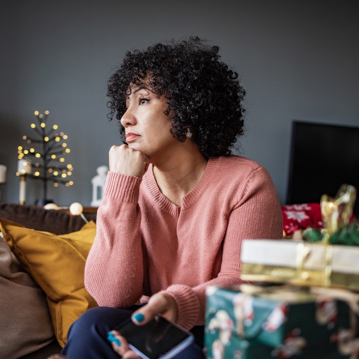 A woman looks sadly out the window at Christmas time.