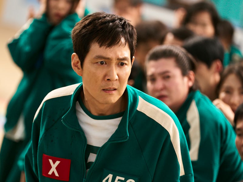 A man in a green prison jumpsuit looks worried amidst a crowd of distressed people in similar attire...