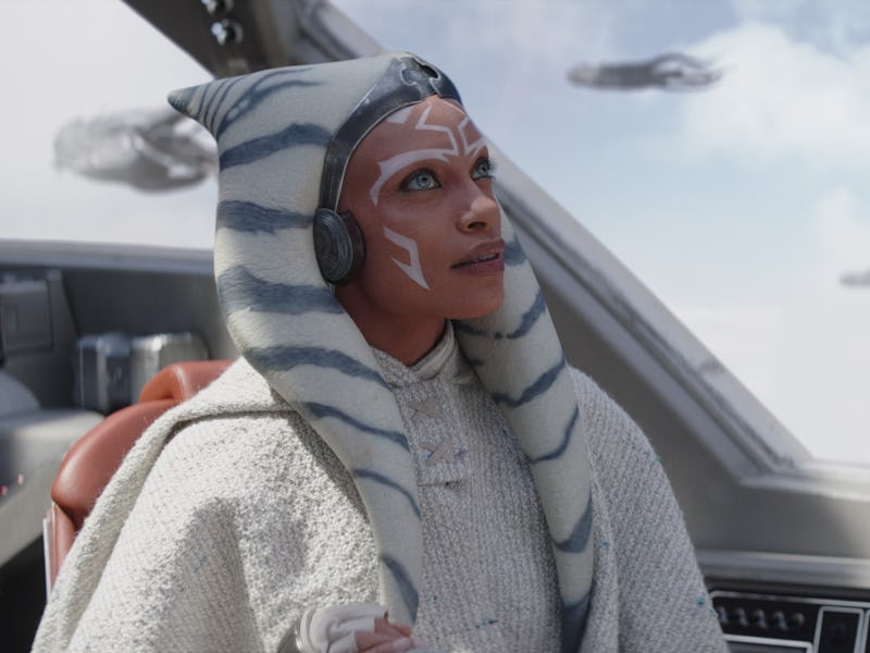 A character with white and blue striped head-tails sits in a spacecraft cockpit, gazing out at dista...