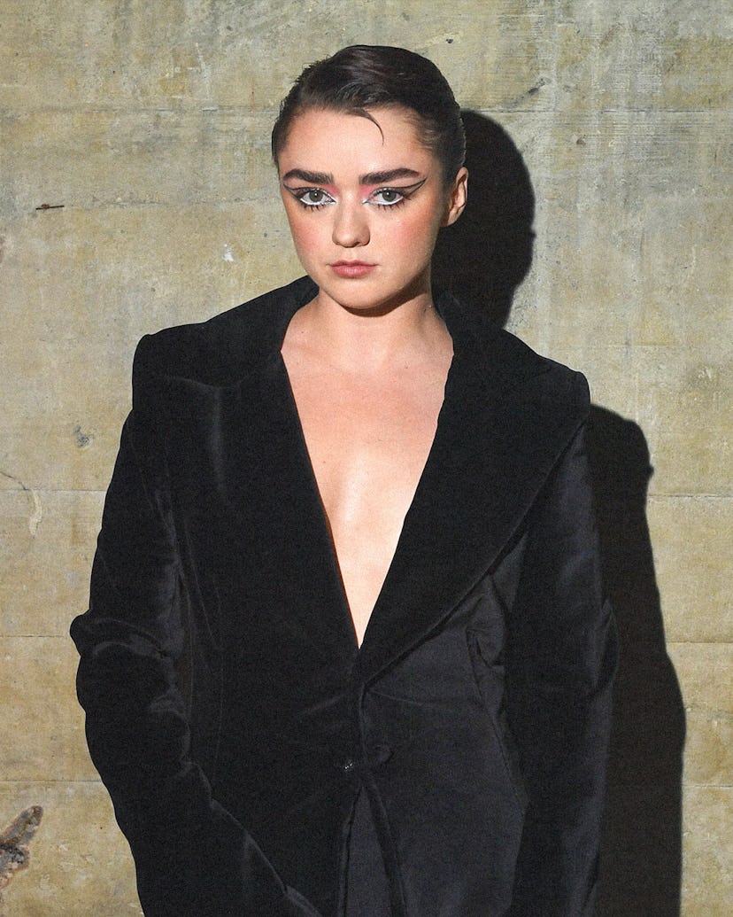 Woman with dramatic makeup wearing a black blazer against a textured wall.