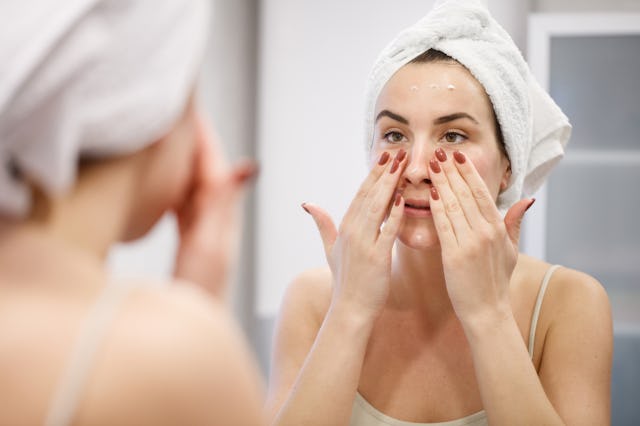 A woman puts cream under her eyes.