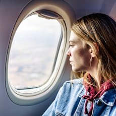 A woman looks out the window of an airplane during her flight.