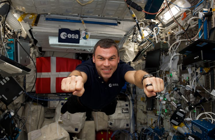 An astronaut wearing a t-shirt floats in microgravity inside the International Space Station. He pos...