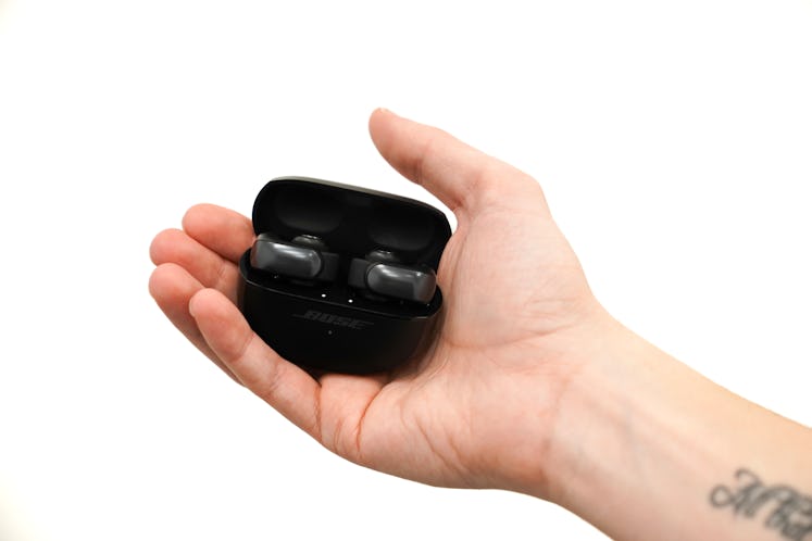 Bose Ultra Open earbuds in a charging case held in a hand.