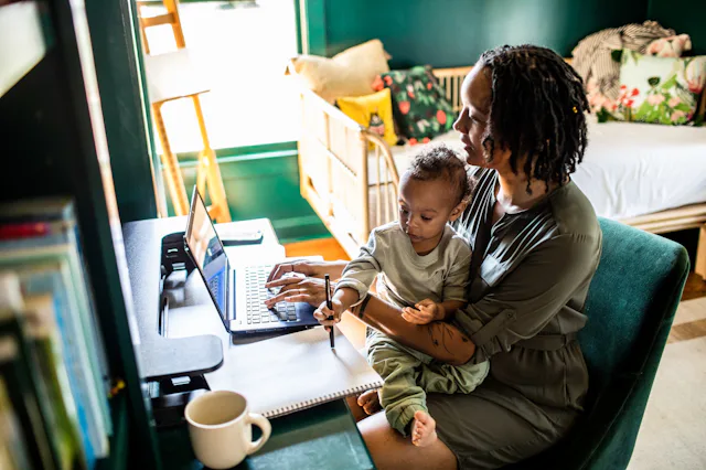 A mom works from home with her young child on her lap.