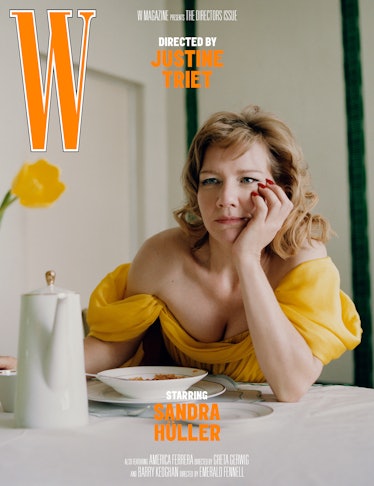 A woman in a yellow top sits at a table with a thoughtful expression, resting her chin on her hand, ...