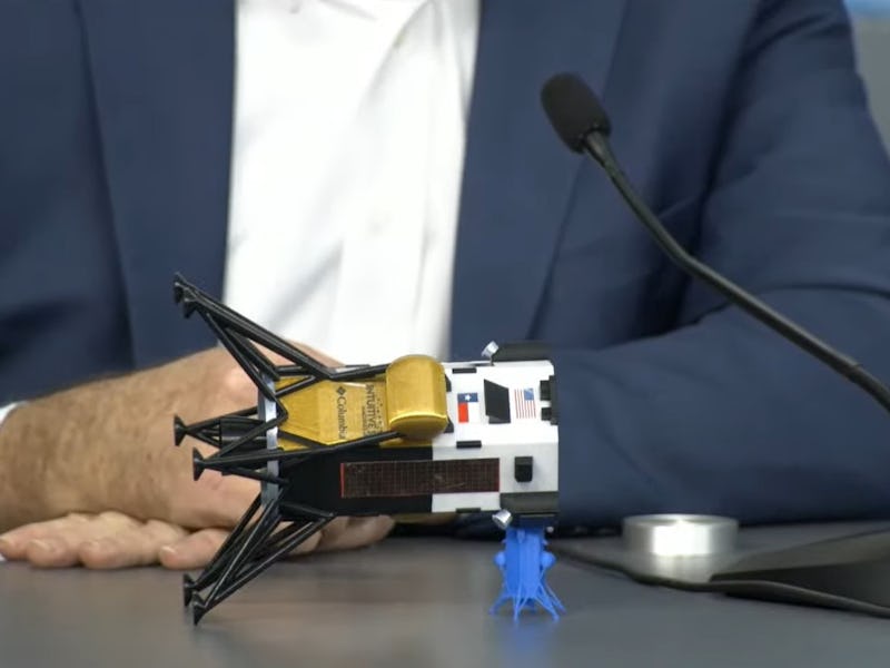 A model Odysseus lander is placed on a desk on its side, with the six legs sticking out on one side,...