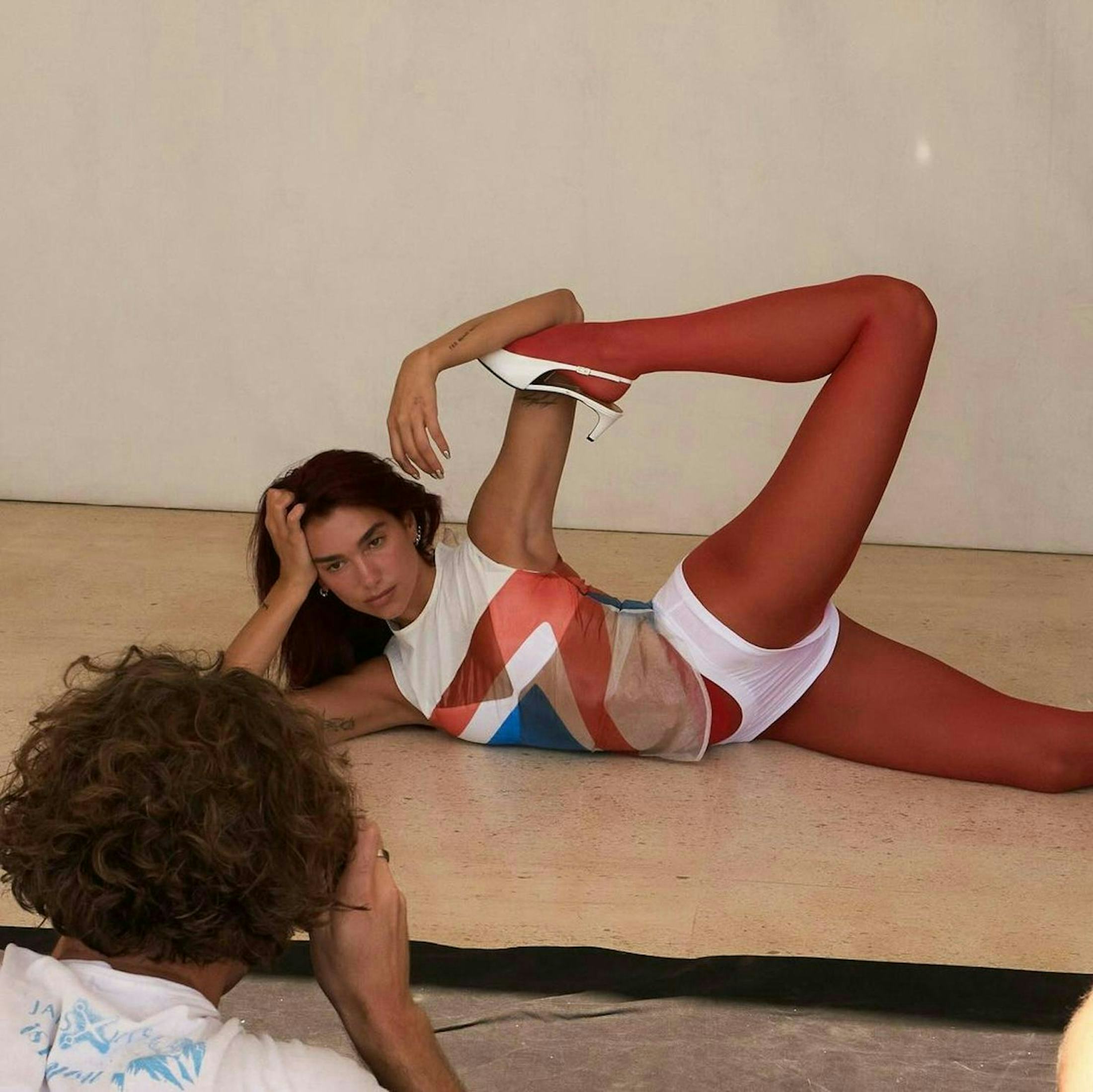 Dua Lipa wears a white tank, tighty whities, and red tights.