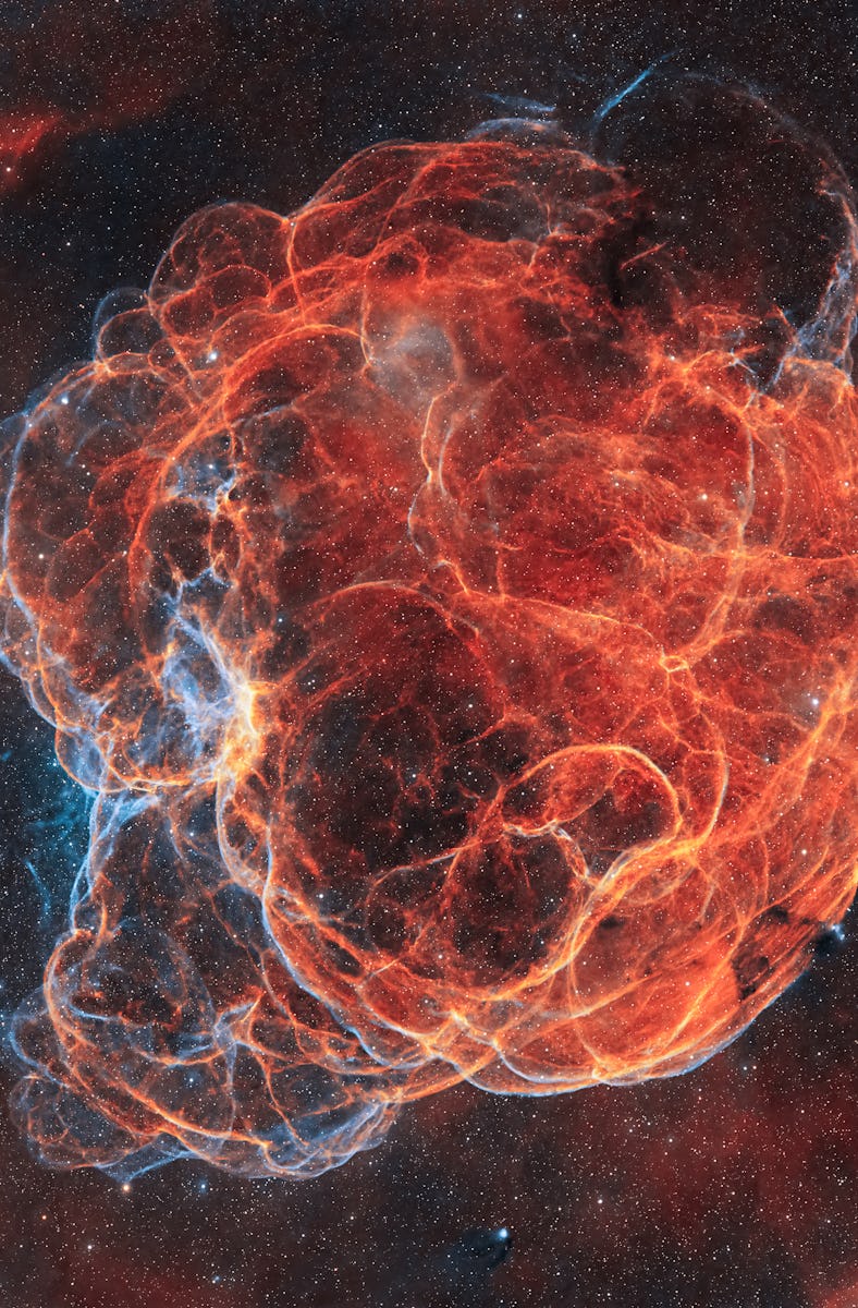 A vibrant celestial image of a red and orange nebula with intricate filament structures, set against...