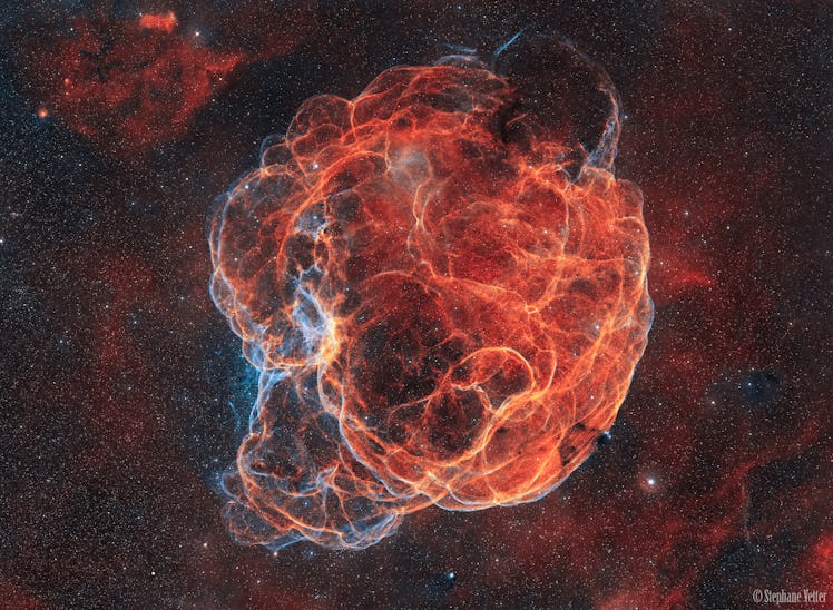 a reddish cloud of gas, laced with curving filaments, with stars in the background