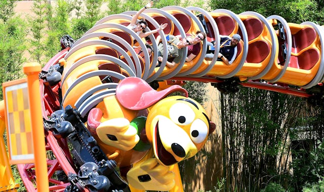 Guests at Disney World ride the Slinky Dog Dash rollercoaster, some of them raising their hands in e...