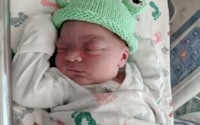 A baby born on Leap Day wears a frog hat.