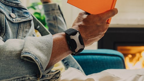 Person in denim jacket holding a book, wearing a black wearable device, with a cozy fireplace in the...