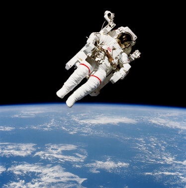 An astronaut flies in space, tilted with the head pointing to the top right. Earth's curved horizon ...