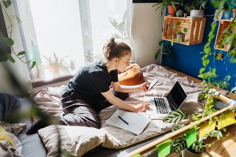 A teen sits in a bedroom with plants.