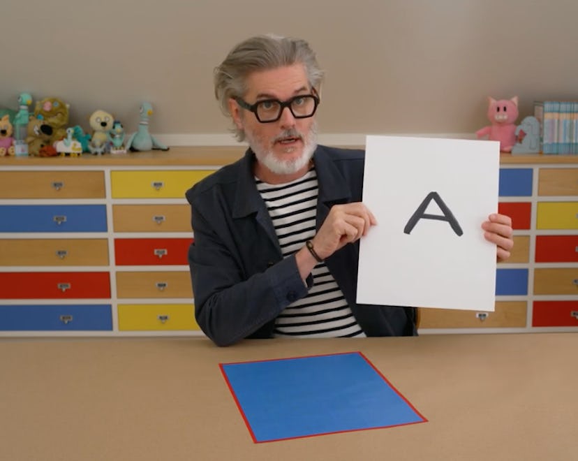 Mo Willems holds up the letter "A" in his art studio -- stuffed animals from his many books are visi...