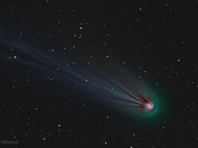 photo of a green comet with a red nucleus and a blue tail, with stars and black sky in the backgroun...