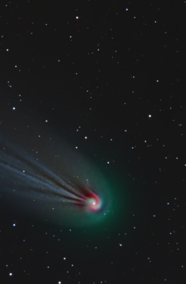 photo of a green comet with a red nucleus and a blue tail, with stars and black sky in the backgroun...