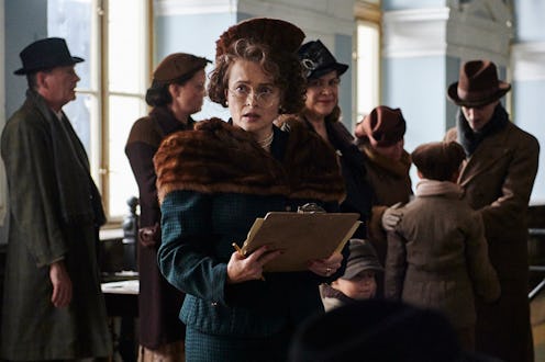 A woman in vintage clothing holds a clipboard with a pensive expression, surrounded by people in a p...