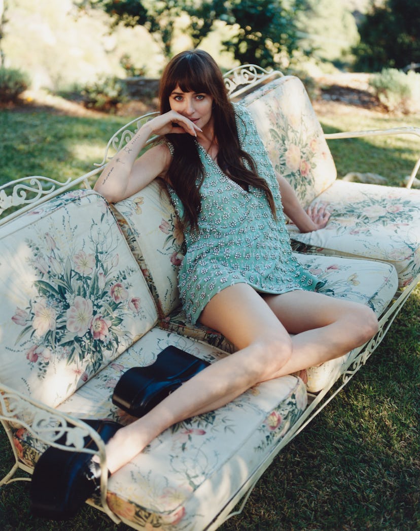 Dakota Johnson reclining on a sofa in a Gucci dress and shoes.