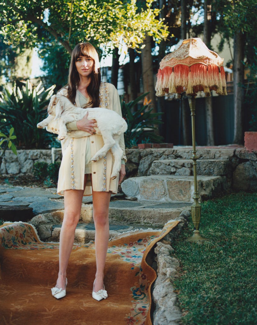 Dakota Johnson carrying a baby goat and wearing Miu Miu clothing for her Bustle shoot.