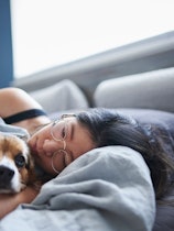 A woman lies in bed sick with her dog.